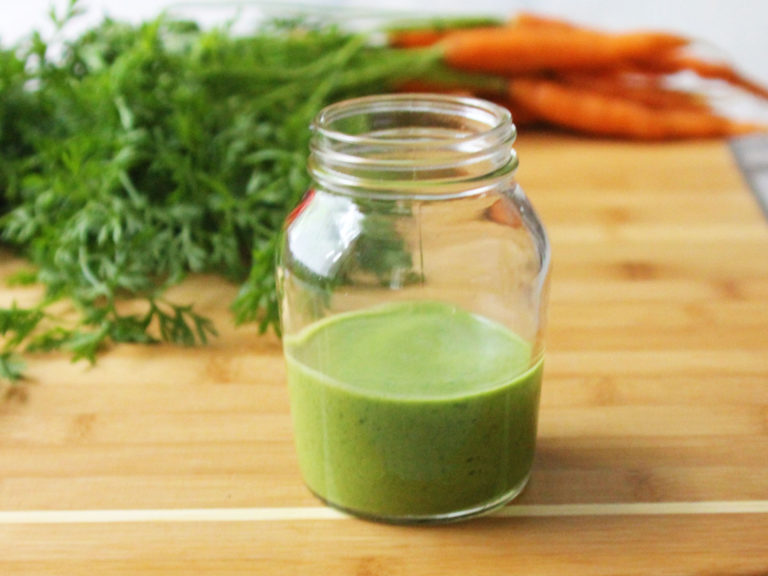 a jar of green Carrot Greens Vinaigrette and a bundle of carrots in the background