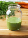 a jar of fresh green dressing with a bundle of carrots in the background