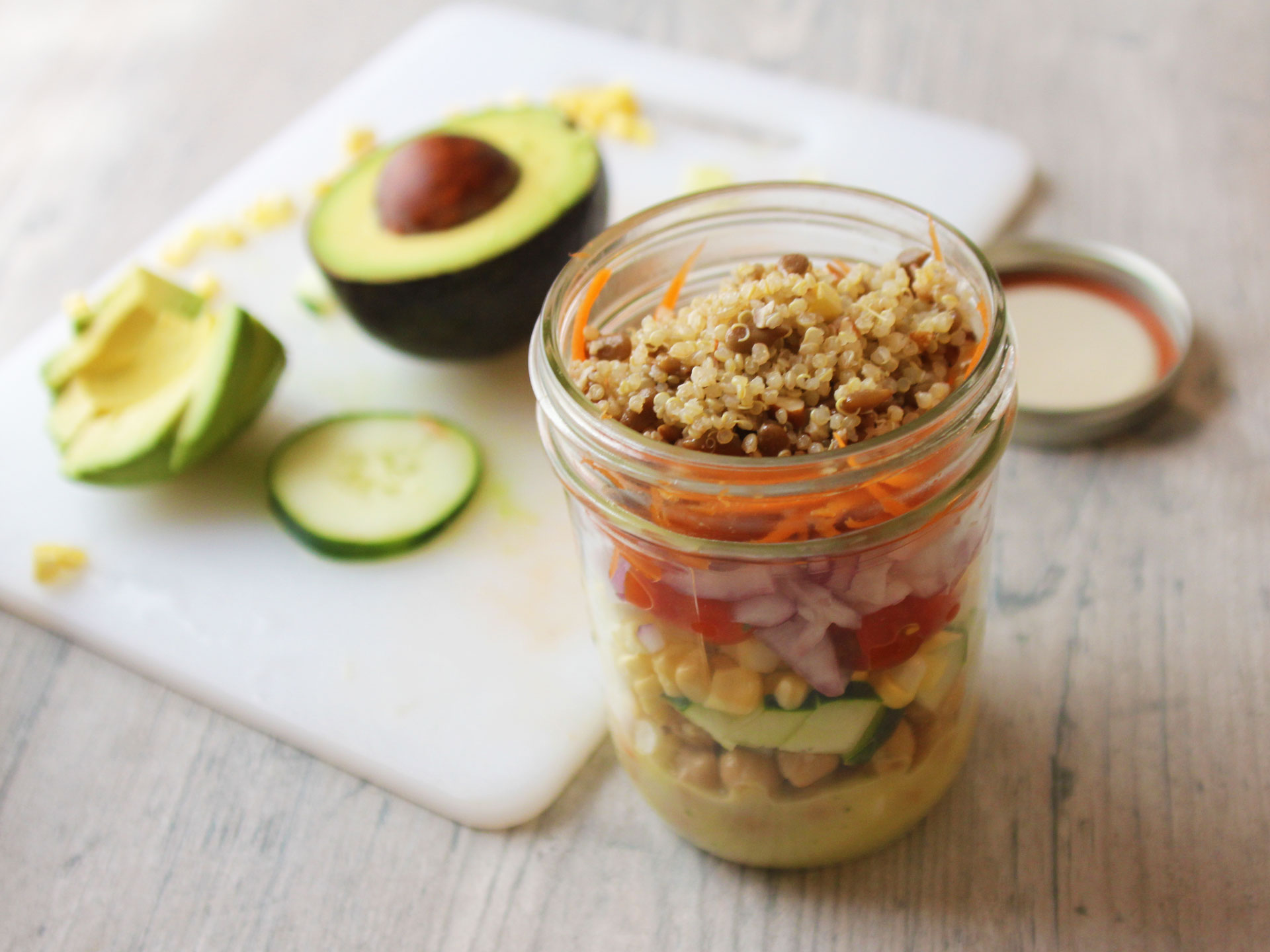 a jar full of salad ingredients with a cut avocado on the side  